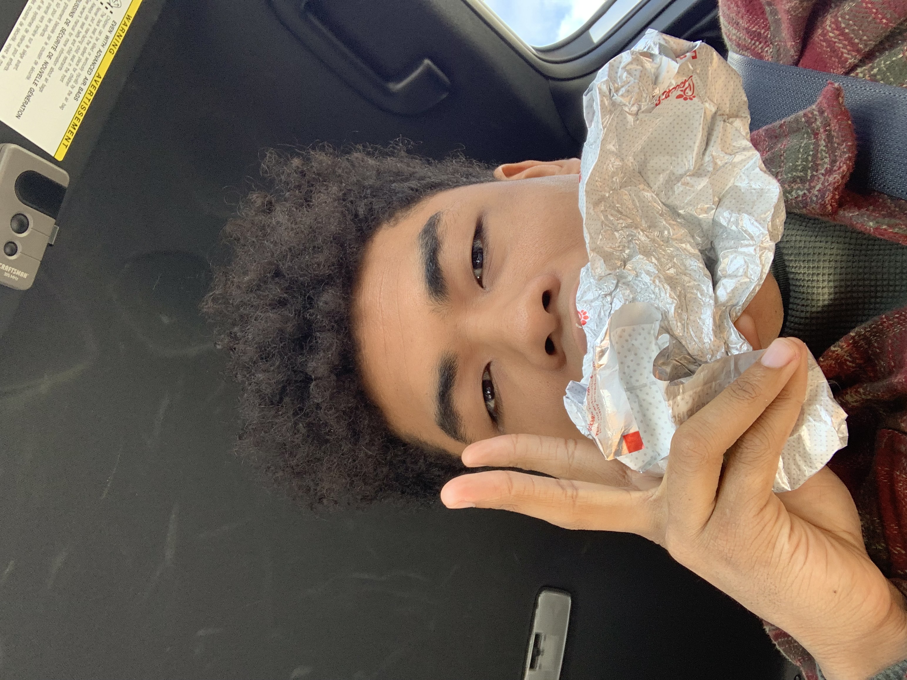 A boy eating a sandwich while holding up two fingers.